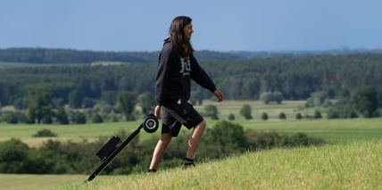 A man carries an electric skateboard on the prairie