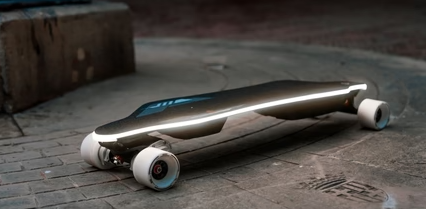 A sleek, futuristic electric skateboard lying on a concrete surface, featuring a streamlined design and LED lights along its length.