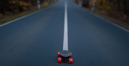 A skateboard positioned on an empty road, with trees lining both sides. 