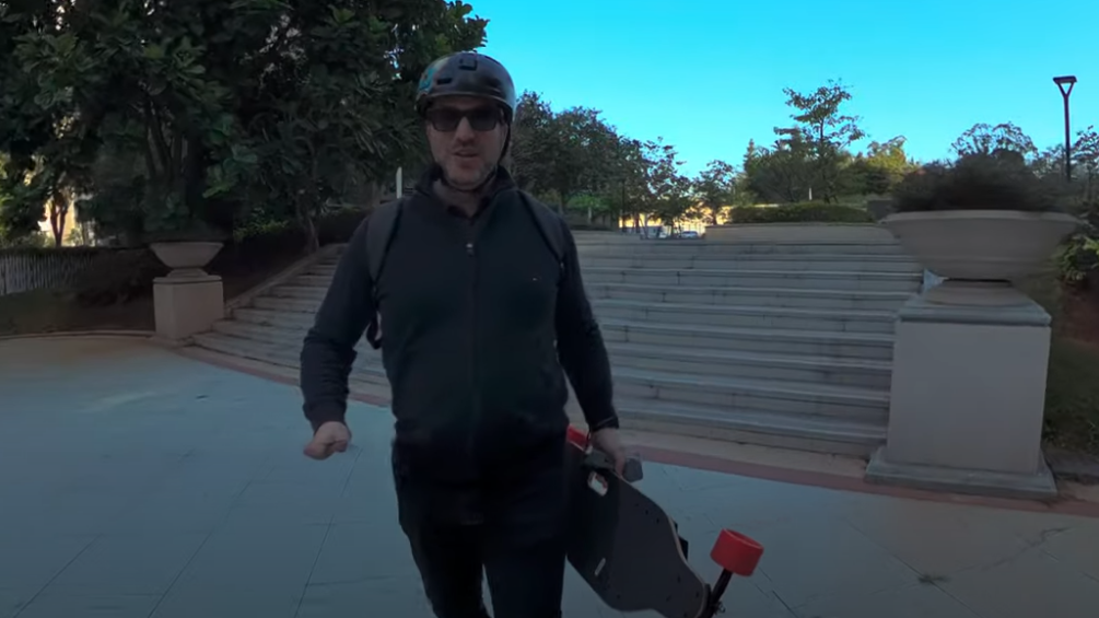 Man in a helmet holds an electric skateboard near steps.