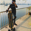 Rider with Meepo electric skateboard by the waterfront, city skyline in background.