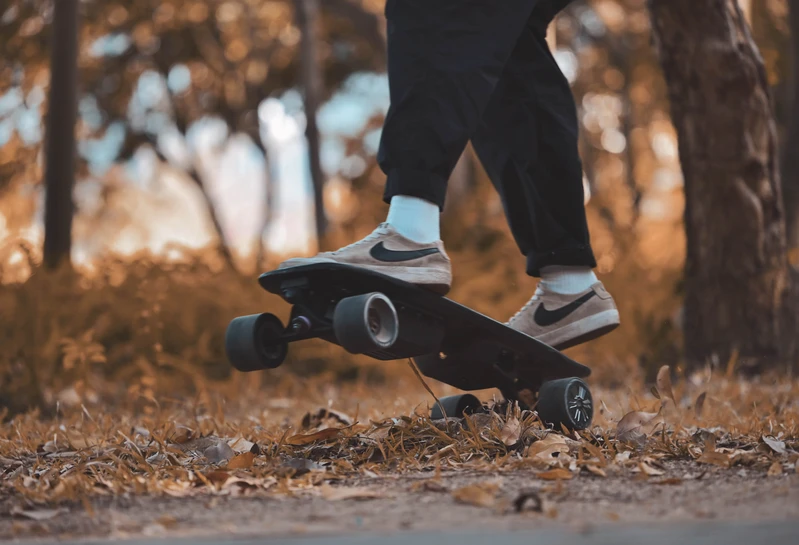 Rider navigating Meepo Atom electric skateboard on a leaf-covered path.