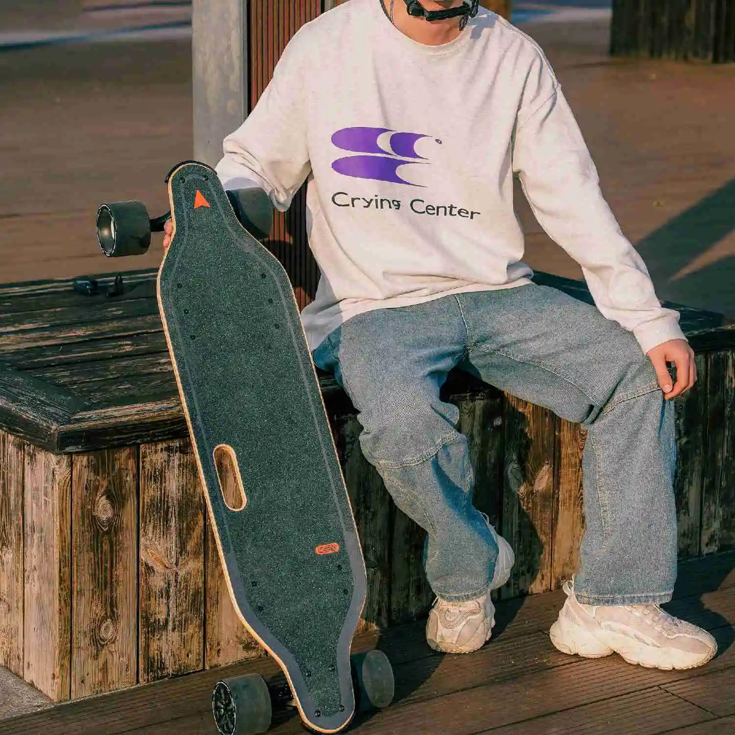 Person in sweatshirt sitting with Meepo skateboard by their side, showcasing urban style.