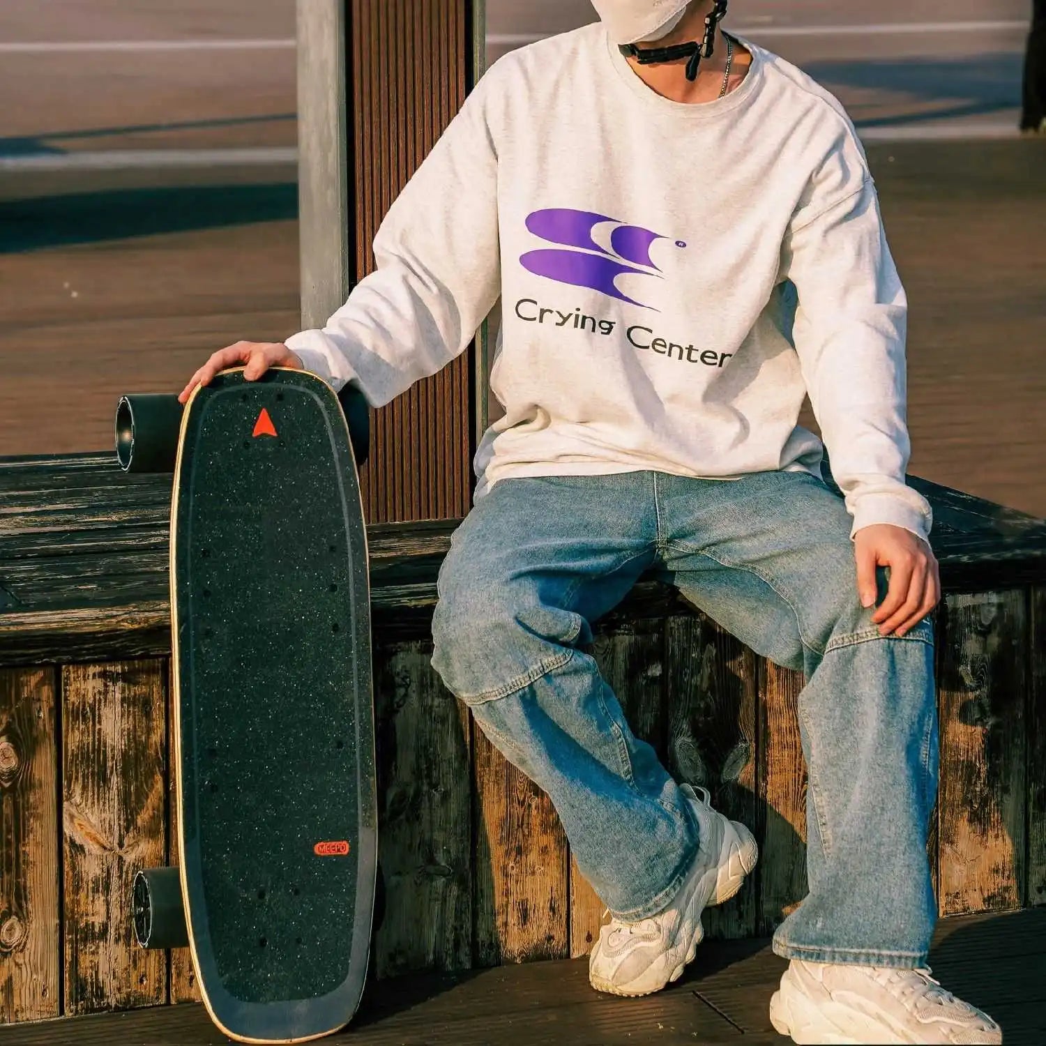 Person seated with Meepo Mini 5 skateboard, wearing a Crying Center sweatshirt.